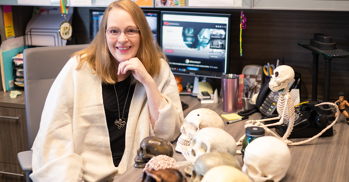 Kelly Peterson sits at her desk with many model skulls.