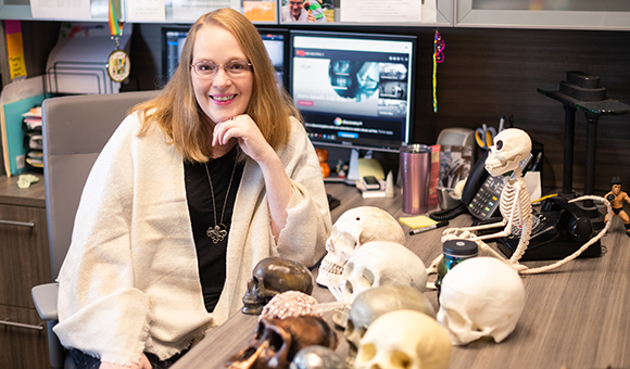 Kelly Peterson sits at her desk with many model skulls.