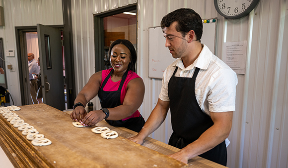 Josiah Martin shows New York State SBDC Director Sonya Smith how to twist pretzels.
