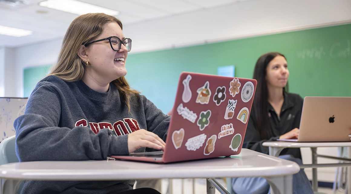 A student with a pink laptop and colorful stickers participates in a marketing class.