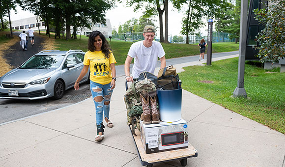 Two students use a cart to transport belongings to their residence hall.