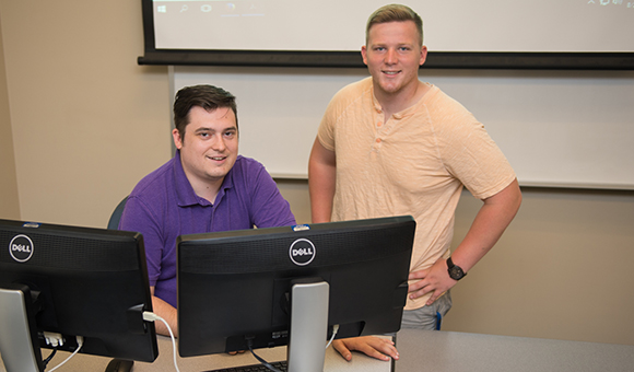 Miles Canino and Heath Boyea sit behind a computer.