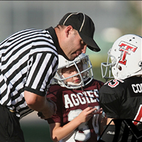 An official leans over to talk with youth football players.