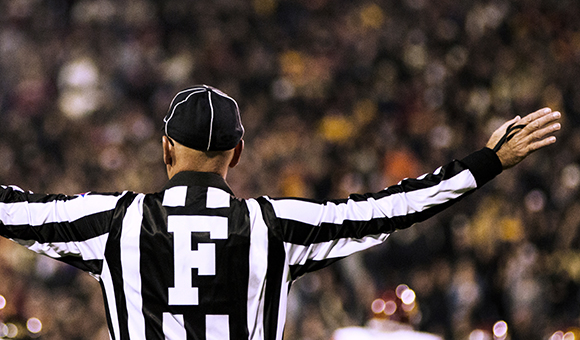 A football official with back facing, holds one arm up during a game.