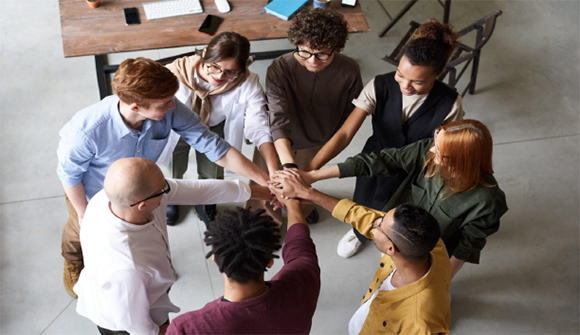 A group collectively puts their hands together in the middle of a circle.