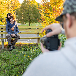 A SUNY Canton student takes a photo of a couple on bench during a photography portrait class.