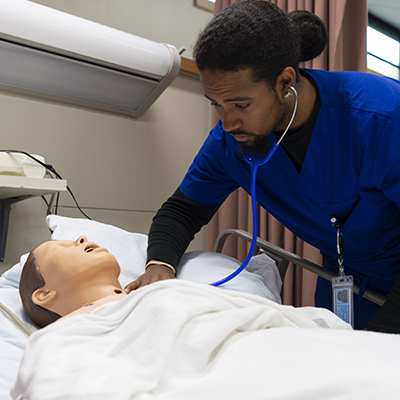 A nursing student checks the pulse and heart rate of a dummy patient.