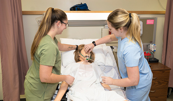 Nursing students Madison Parker and Abby Stiles affix an oxygen mask to one of the college's learning mannikins.