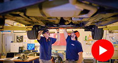 Two students work underneath a lifted car.