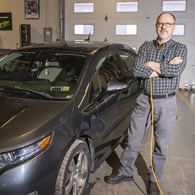 Brandon Baldwin stands next to an electric vehicle in the Automotive lab.