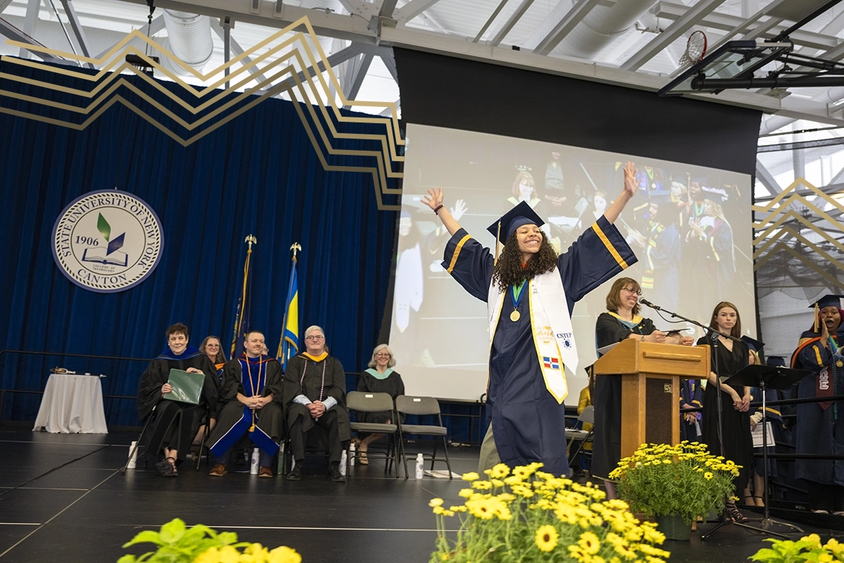 A graduate celebrates with arms up while walking across the Commencement 2024 stage.