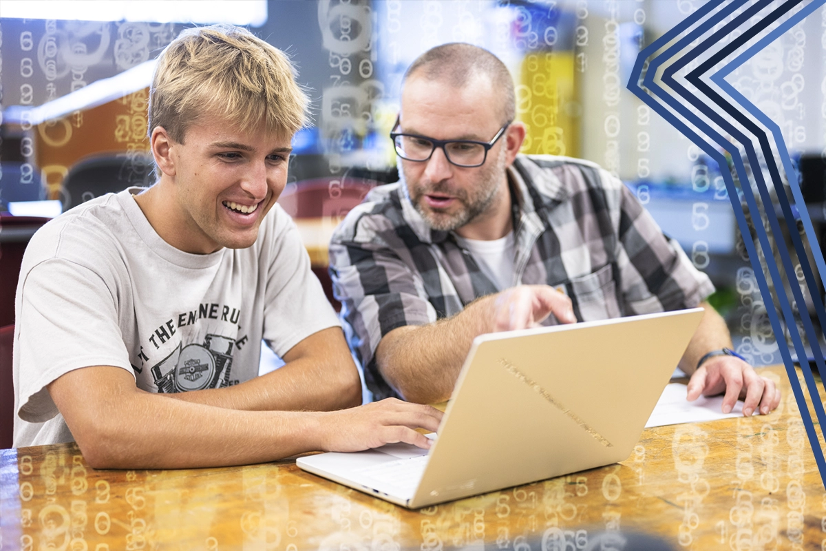 Professor Lucas Craig works with a student on a laptop in the Mechanical lab.