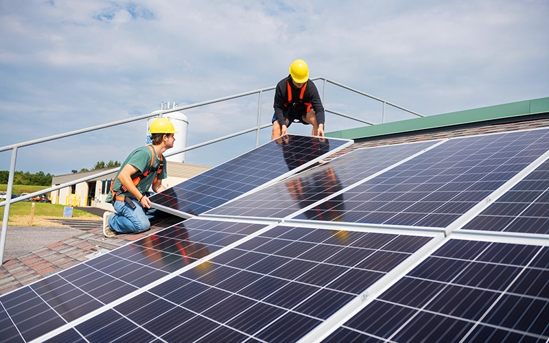 Two students install solar panels on a mock roof.