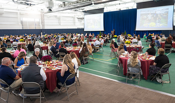 Dozens of tables consisting of students and donors watch Vice President Tracey Thompson deliver the Scholarship Luncheon program.