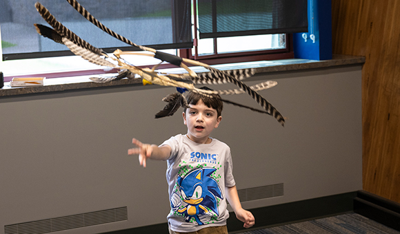 An elementary-aged camper throws a feather invention into the air.