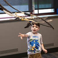 An elementary camper throws a feather invention into the air.