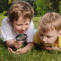 Two children viewing grass through a magnifying glass.