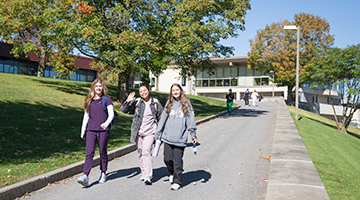 Three students walk down the ramp near Nevaldine Hall.