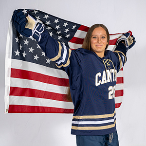 A women's hockey player holds up an American flag behind her.