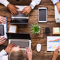 People on laptops collaboratively work at a conference table.