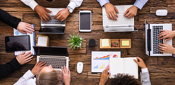 People on laptops collaboratively work at a conference table.