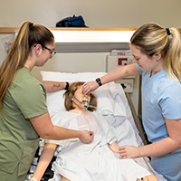 Two nursing students check the breathing of medical dummy.